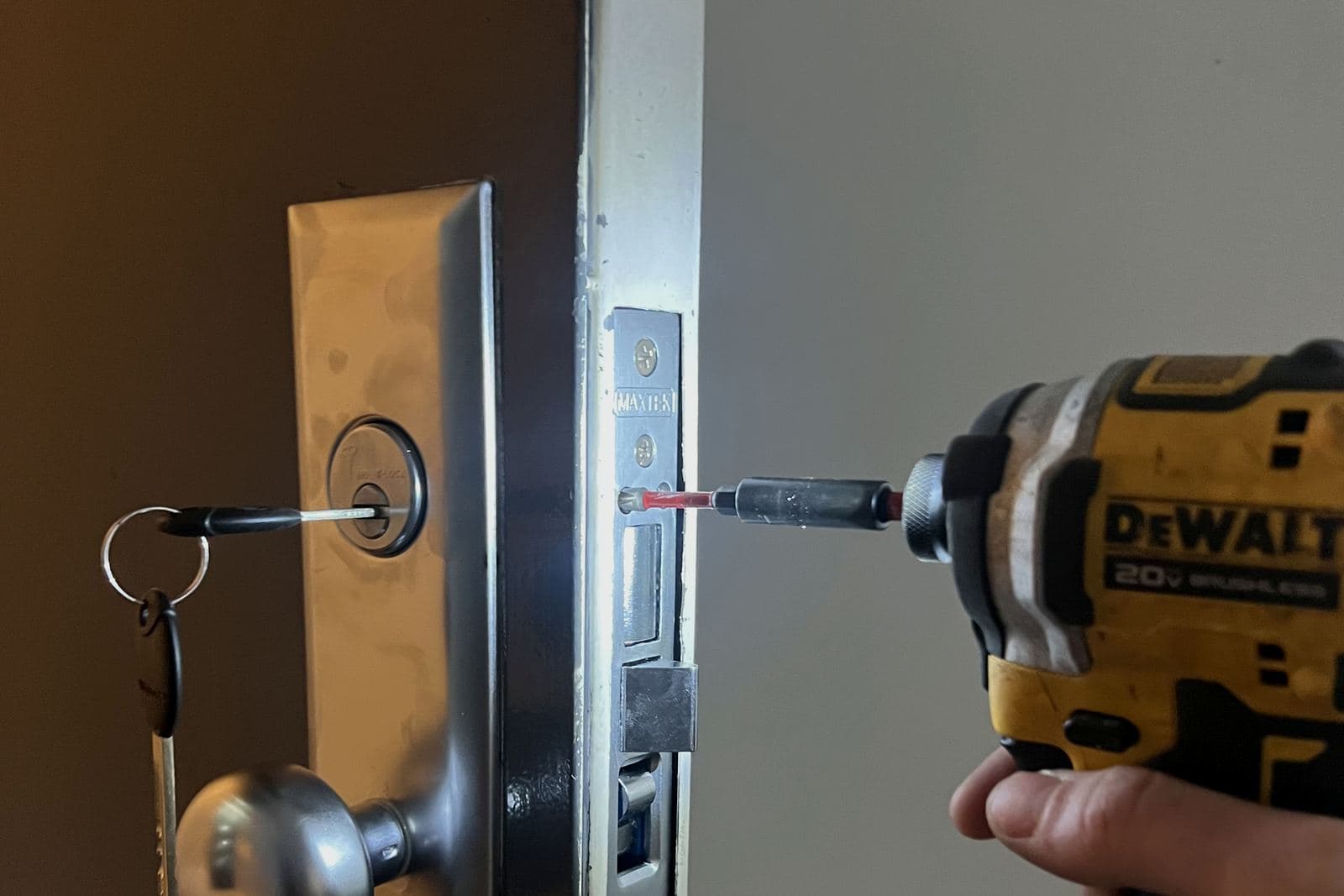 Cordless impact driver at the latch plate of a steel door with a key in the lock cylinder